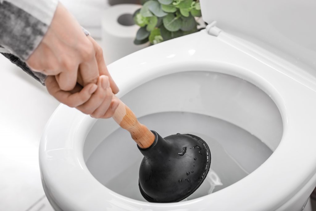 Young woman using plunger to unclog a toilet bowl