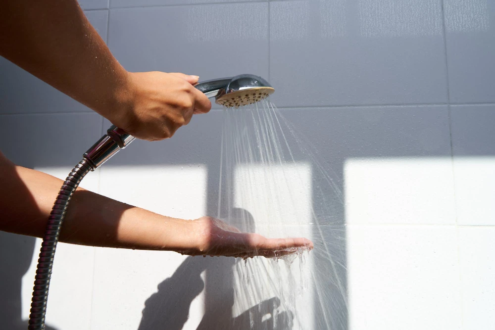 Female hand touching water pouring from a rain shower head checking water temperature
