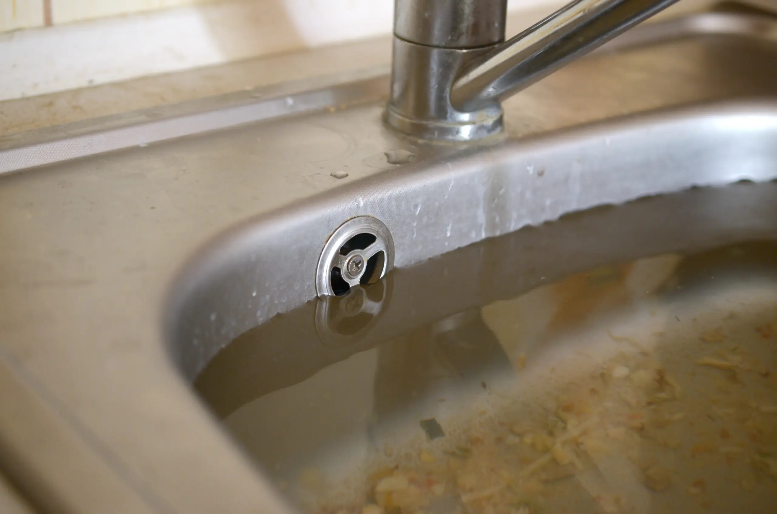 stainless steel sink overflowing and clogged drain, full of water and particles of food